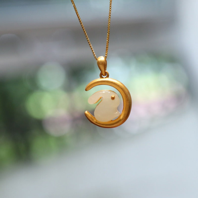 a gold chain with a pendant, which features a gold moon adorned with a white jade rabbit.